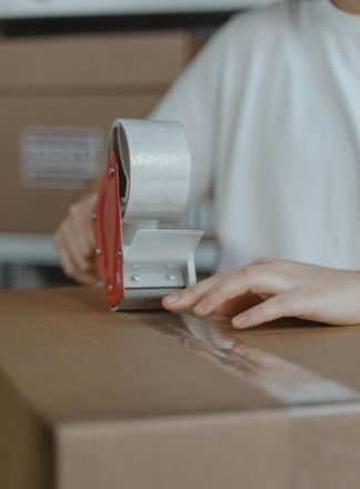 A person sealing a cardboard box with a tape dispenser in an indoor setting.